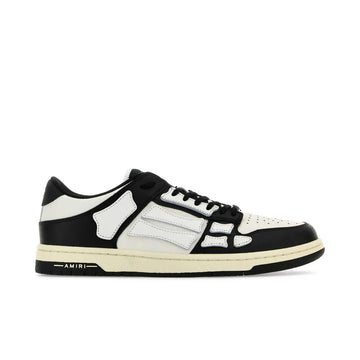 A pair of low-top white and black sneakers by AMIRI, available at Lestyle Boutique. These sneakers feature skeleton-inspired stitching, designer logo details, and a flat sole for comfort and a unique style.