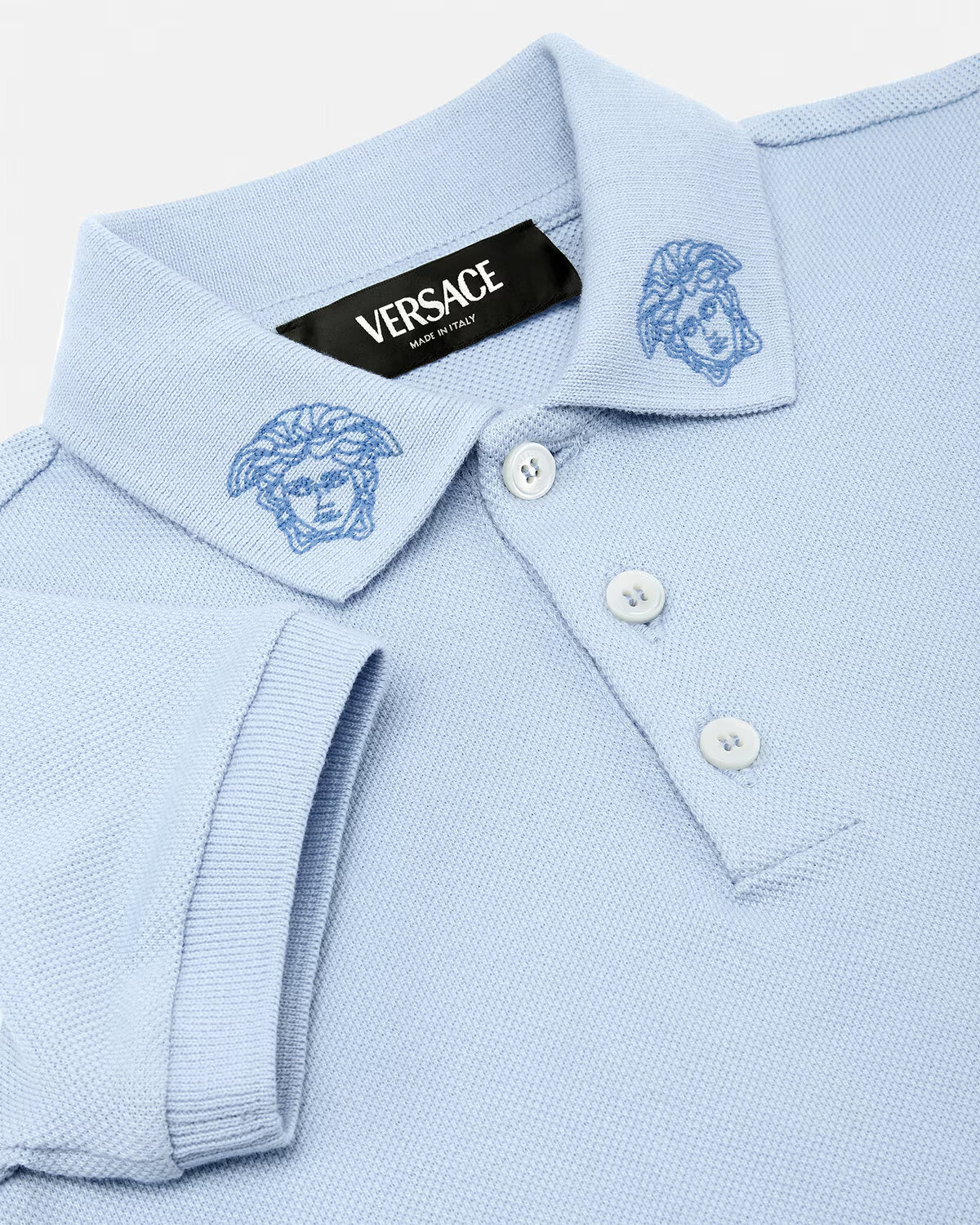 The Versace Embroidered Medusa Baby Polo Shirt from Lestyle Boutique in a charming light blue colour featuring the iconic Medusa Kids embroidery on the collar, short sleeves, a pointed collar, and a three-button placket.