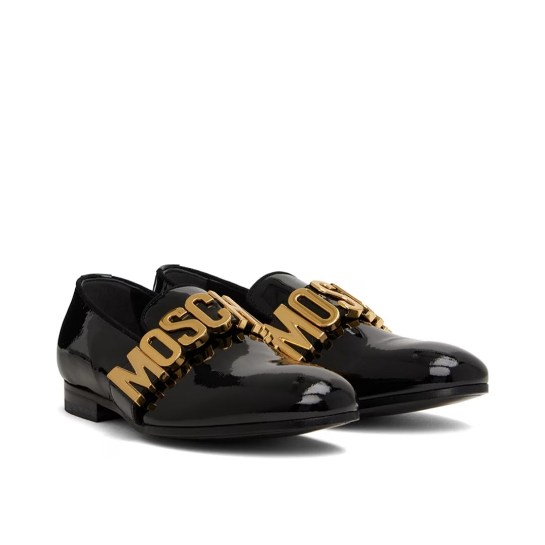 Moschino black lacquered leather loafers featuring gold-tone metal logo hardware across the vamp, a satin collar detail, and a leather and rubber sole, available at Lestyle Boutique 136 Little Collins St.
