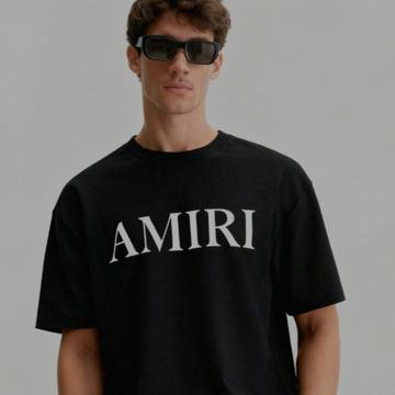 Person wearing a black AMIRI t-shirt against a gray background