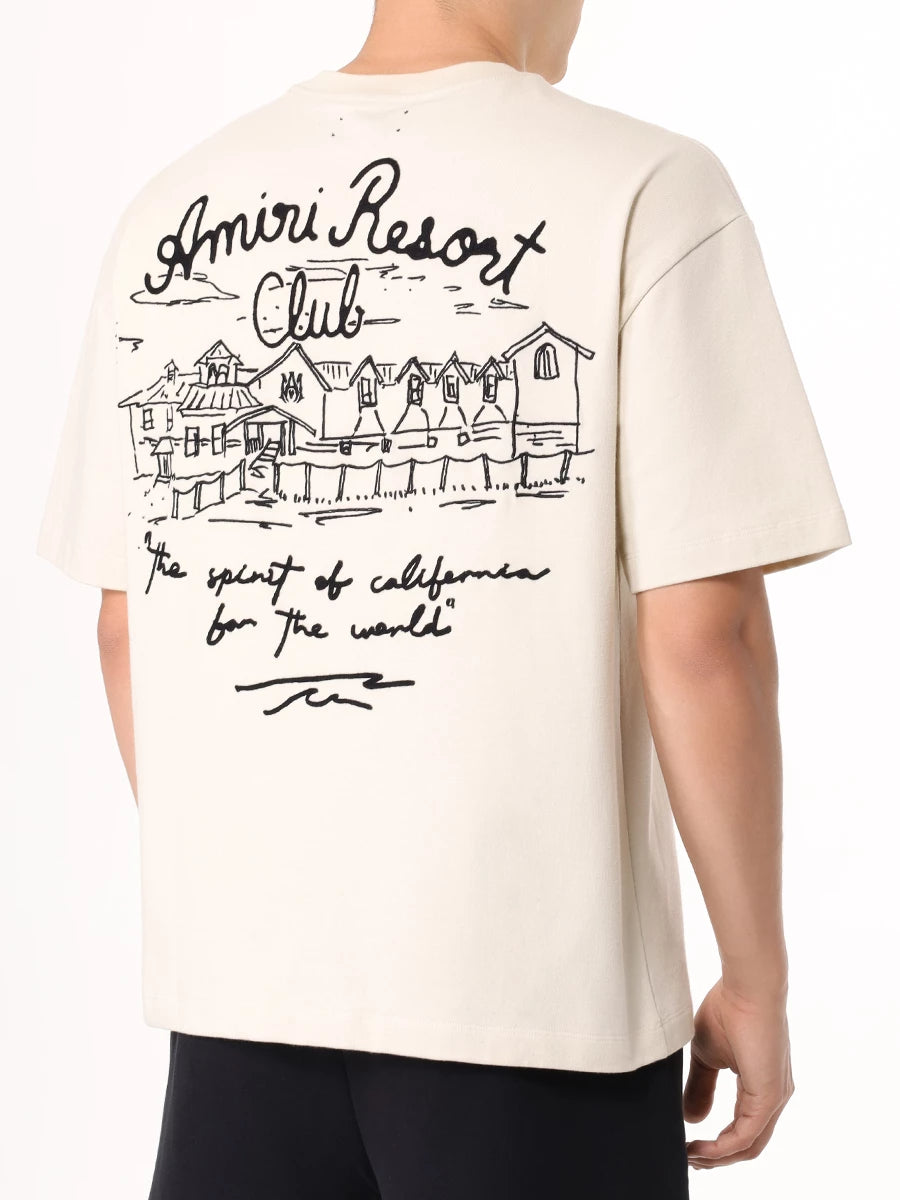 A beige stretch-cotton t-shirt by AMIRI, available at Lestyle Boutique. Featuring embroidered logos on the chest and back, this tee combines comfort and elegance with a resort-inspired aesthetic.