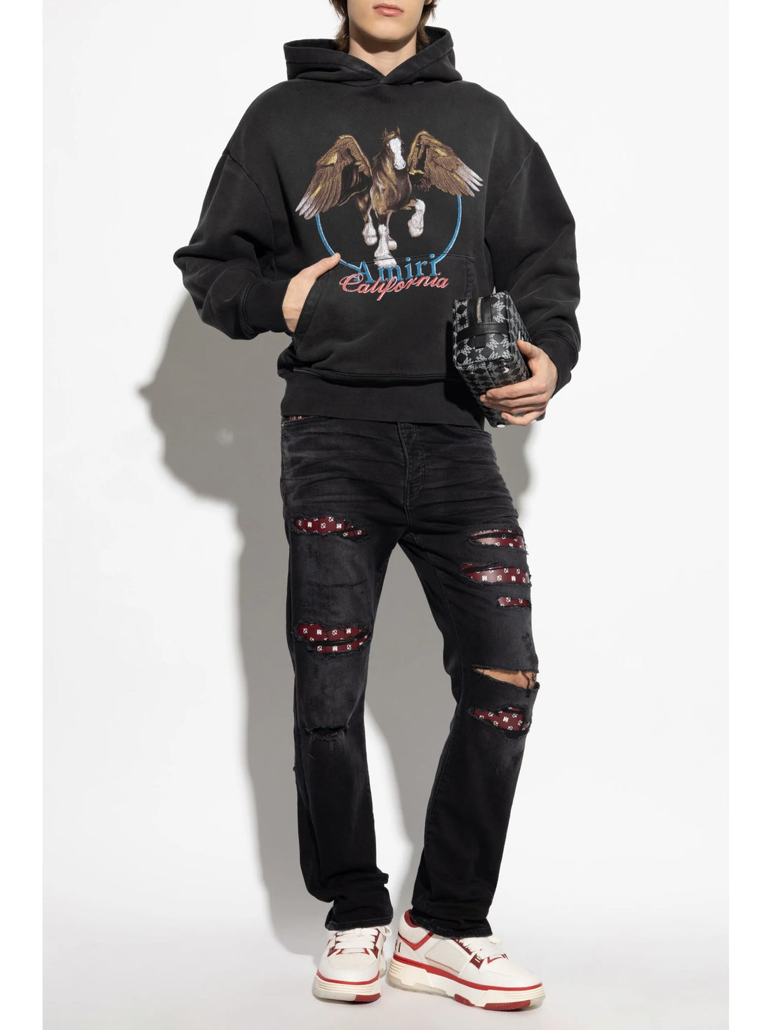 A pair of black distressed jeans by AMIRI, available at Lestyle Boutique. These jeans feature unique bandana inserts, a straight-leg fit, concealed button fastening, and a classic five-pocket design.