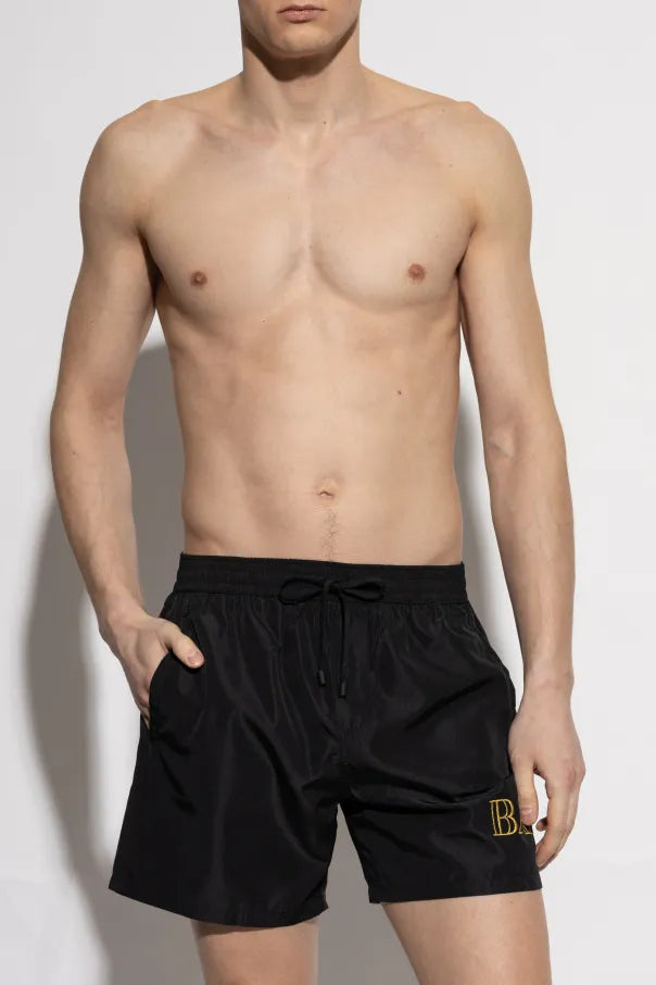 Balmain black swim shorts featuring a distinctive gold logo, made from high-quality glossy polyester, ideal for beach adventures and relaxation. Available at Lestyle Boutique Melbourne.