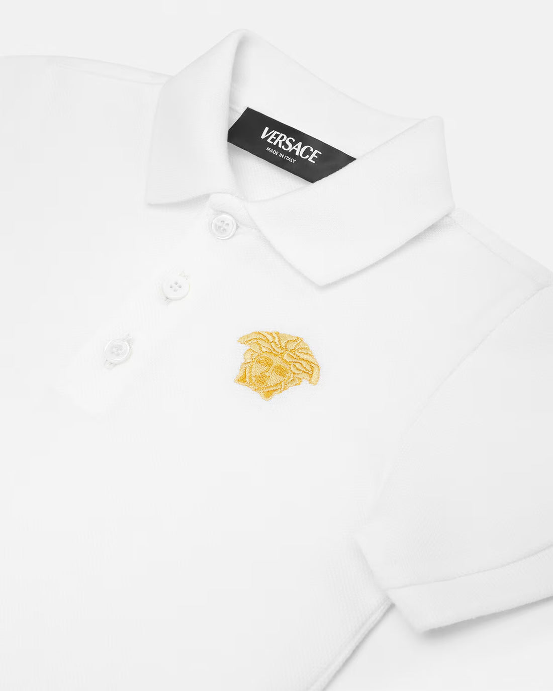 The Versace Embroidered Medusa Baby Polo Shirt from Lestyle Boutique in a clean white colour with a printed iconic Medusa motif embroidered on the chest, featuring short sleeves, a pointed collar, and a three-button placket.