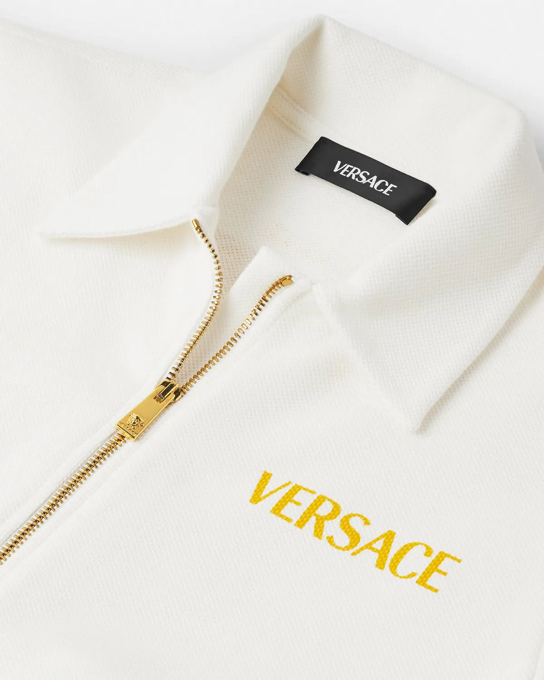 Versace Medusa Garland Kids Zip Polo Shirt in white, featuring long sleeves, a pointed collar, a front zip closure, and signature Medusa Garland detailing, available at Lestyle Boutique.