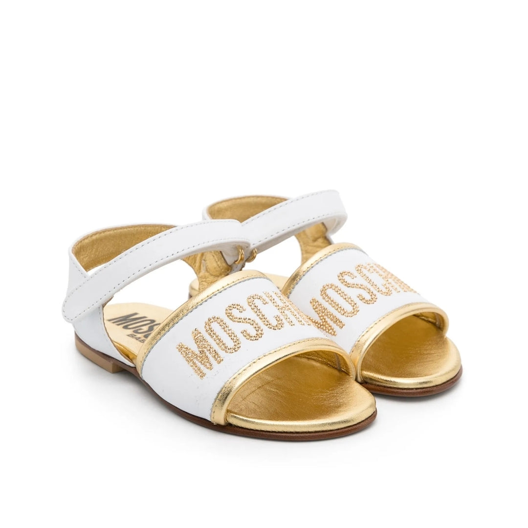 Moschino Kids white and gold calf leather sandals with logo rhinestone embellishment, open toe, and ankle touch-strap fastening, Made in Italy, available at Lestyle Boutique 136 Little Collins St.