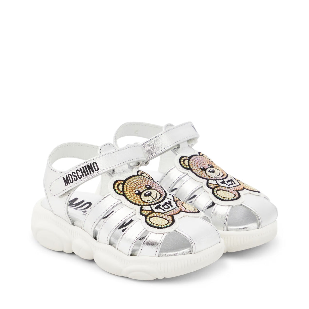 Moschino Kids metallic silver leather sandals featuring a Teddy Bear appliqu??, round toe, and Velcro ankle strap, available at Lestyle Boutique 136 Little Collins St.
