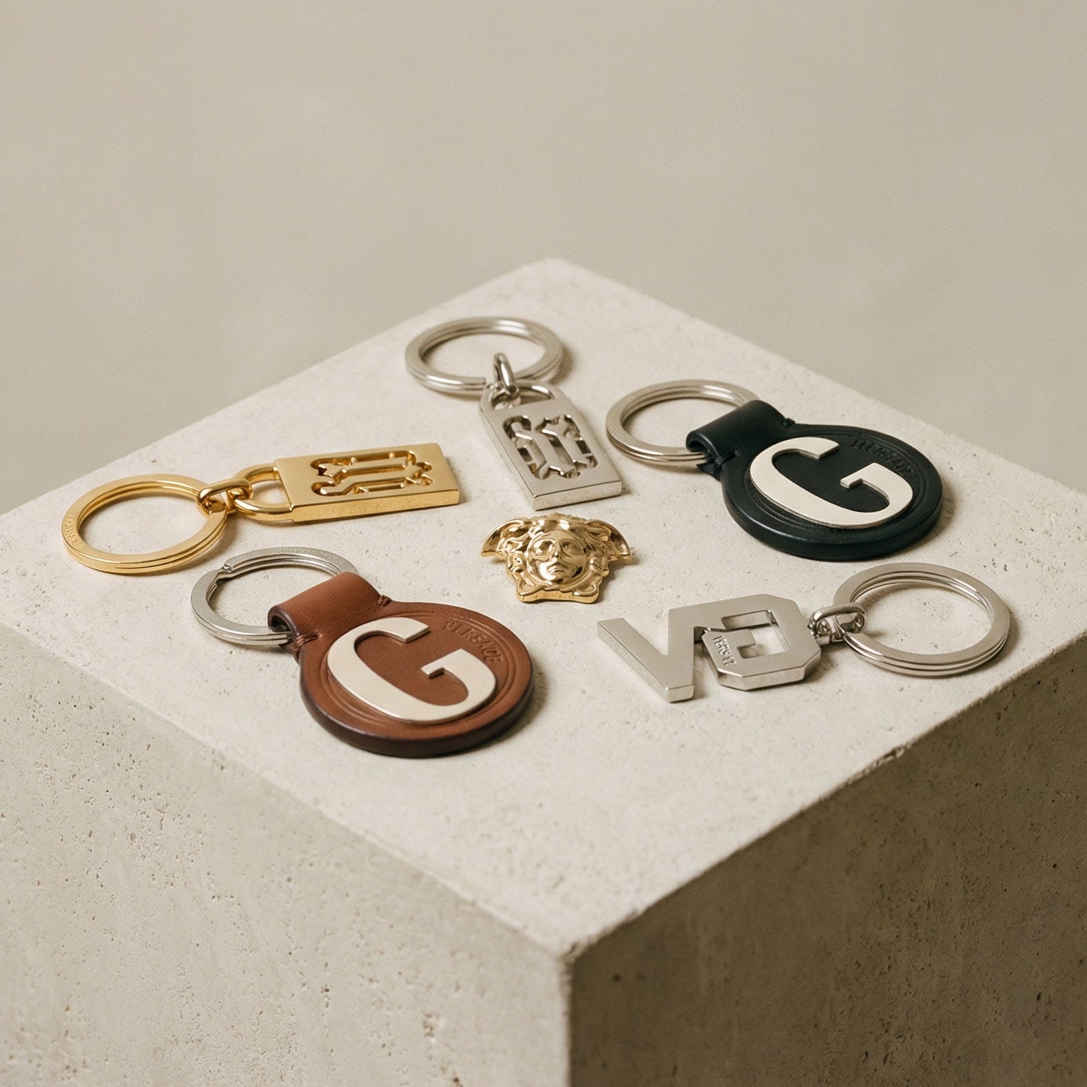 Collection of Versace keychains with 'G' logo on a concrete block