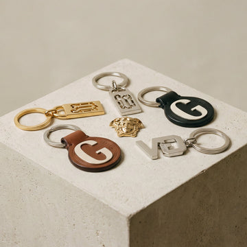 Collection of Versace keychains with 'G' logo on a concrete block