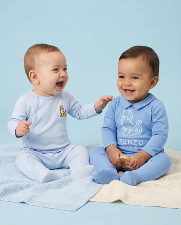 Two babies in blue outfits with a Kenzo logo on a light blue background