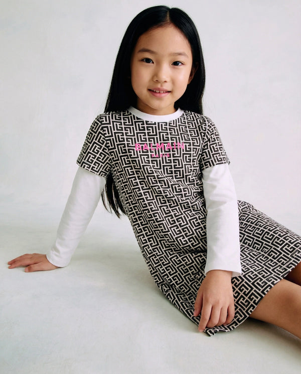Young girl wearing a patterned dress with a white shirt underneath on a plain background