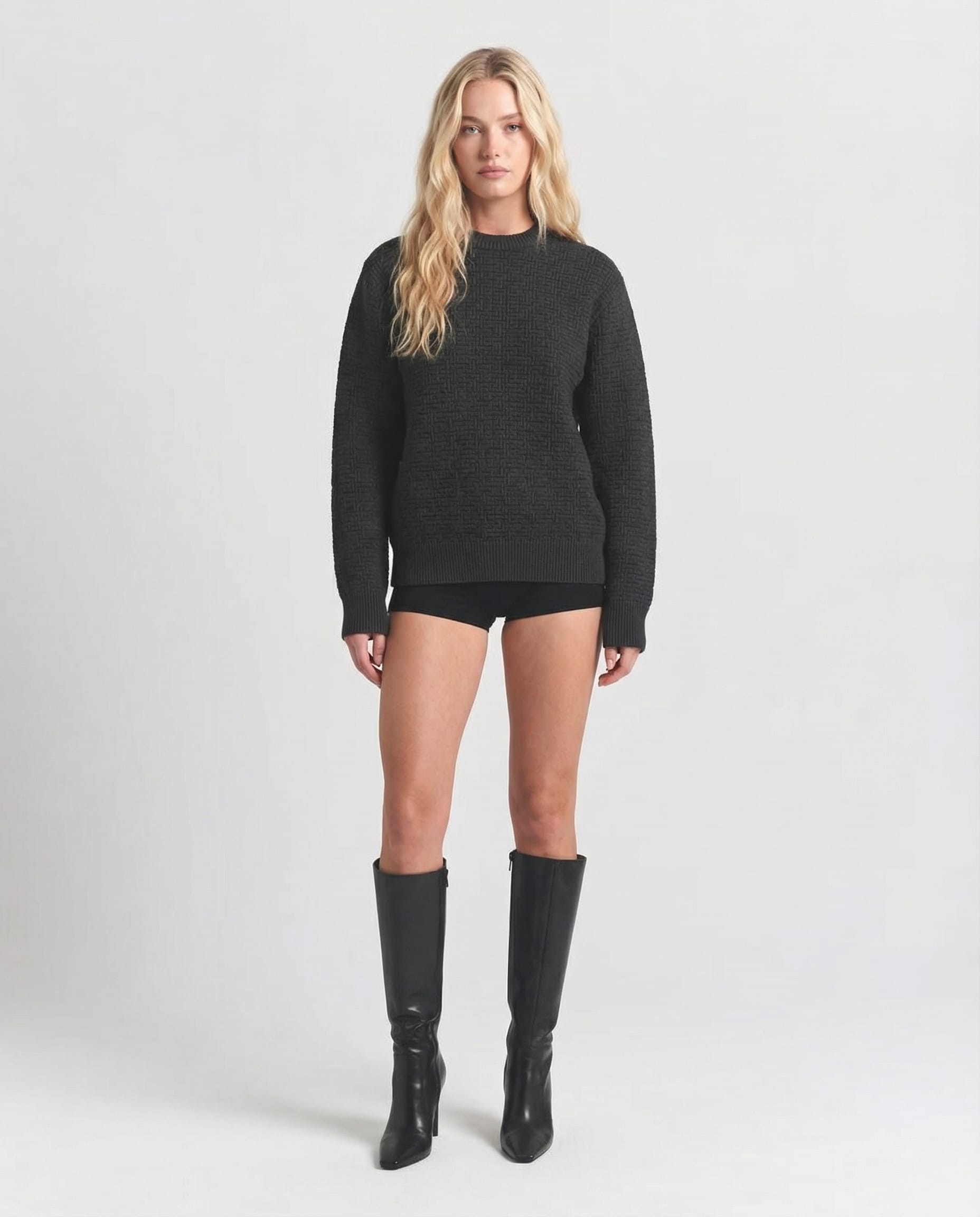 Person wearing a Balmain black sweater and knee-high boots on a white background