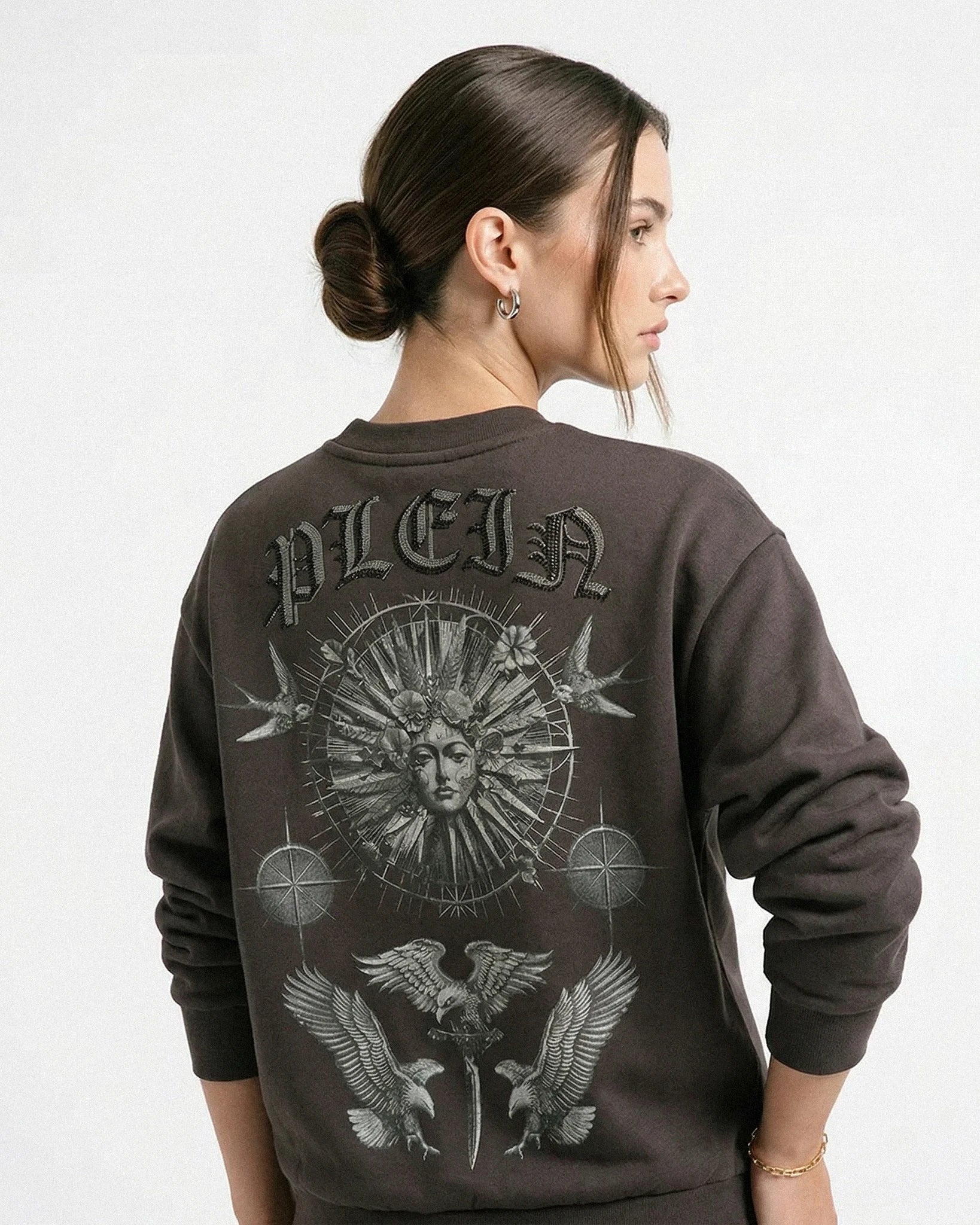 Person wearing a dark gray sweatshirt with intricate designs and 'PLEIN' branding on the back.