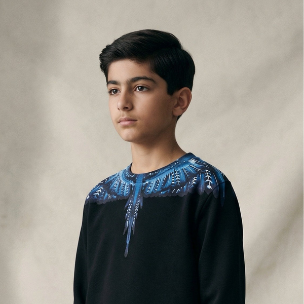 Young boy wearing a black sweater with blue embroidery on a beige background