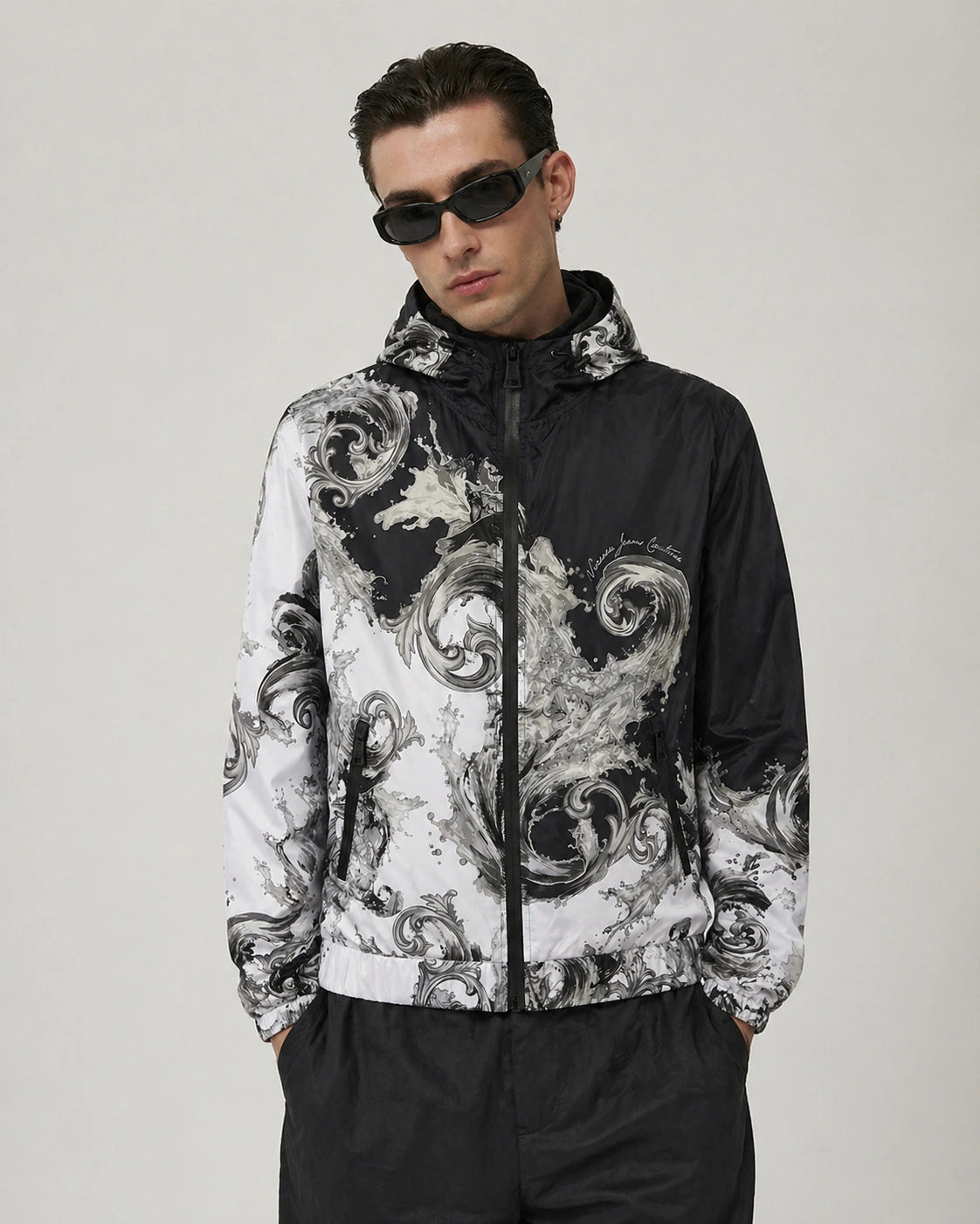 Man wearing a black and white patterned Versace Jeans Couture jacket on a plain background
