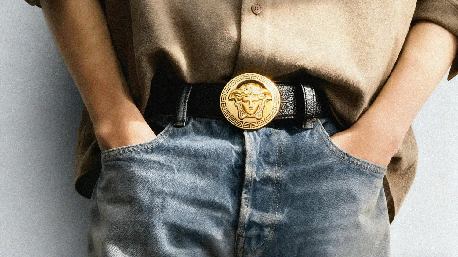 Person wearing a gold belt with a prominent buckle, standing against a neutral background