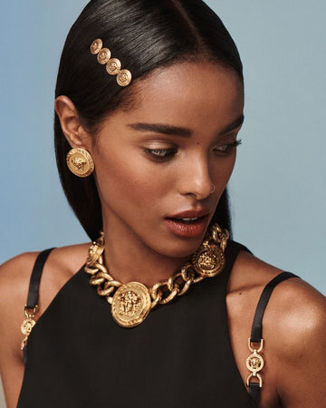 Woman wearing gold jewelry including earrings, necklace, and headband against a blue background