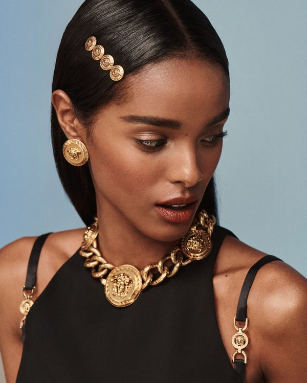 Woman wearing gold jewelry including earrings, necklace, and headband against a blue background