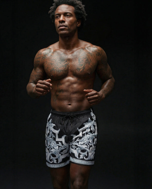 Man with tattoos wearing patterned shorts against a black background
