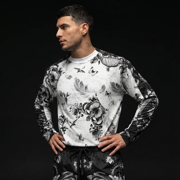 Man wearing a black and white floral patterned versace jeans couture outfit on a black background