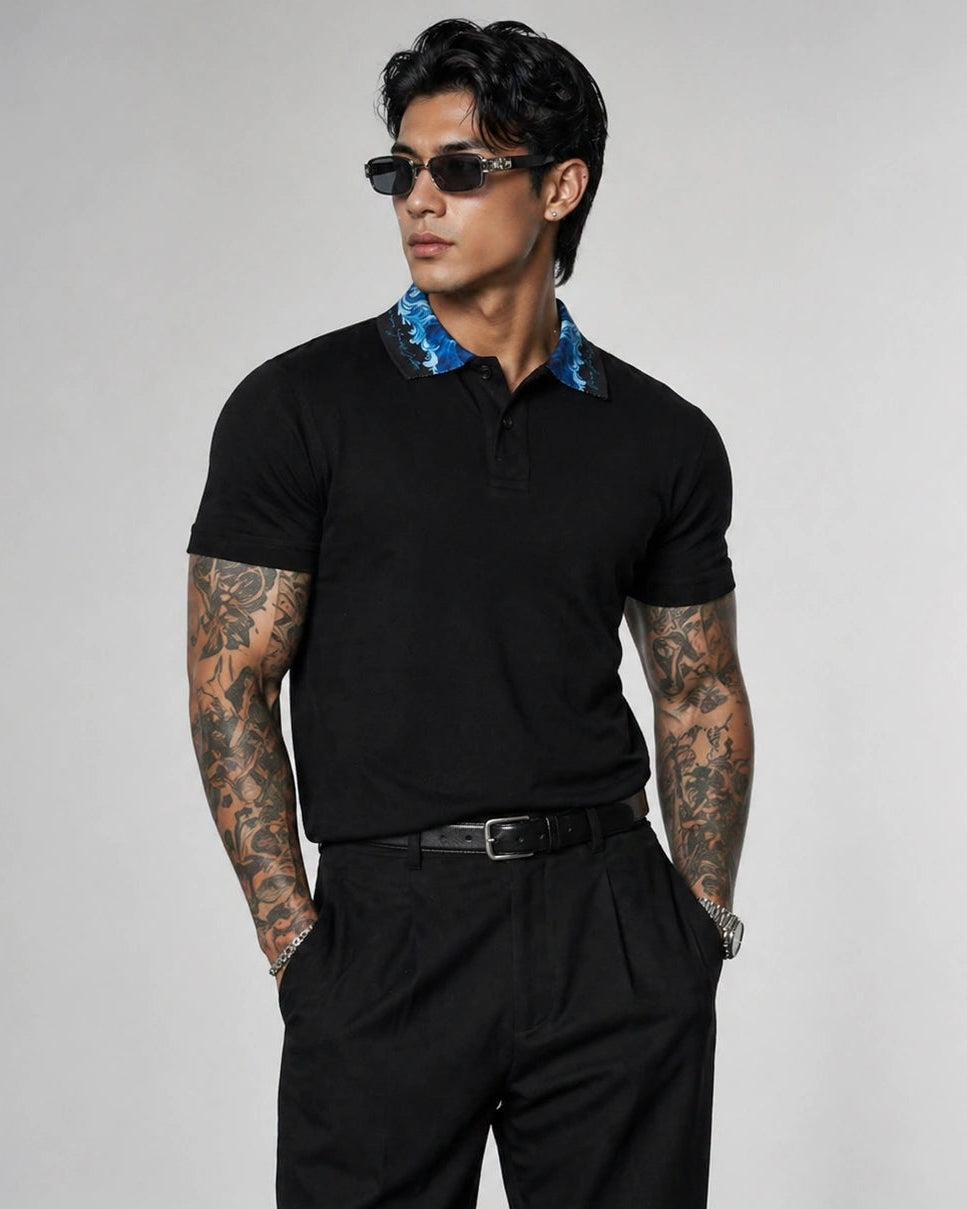 Man wearing a black polo shirt with blue collar and black pants on a gray background