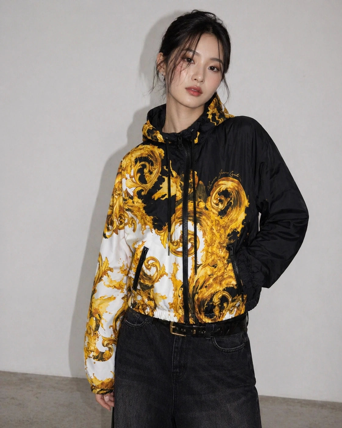 Person wearing a black and gold Versace Jeans Couture patterned jacket against a plain background