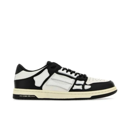 A pair of low-top white and black sneakers by AMIRI, available at Lestyle Boutique. These sneakers feature skeleton-inspired stitching, designer logo details, and a flat sole for comfort and a unique style.