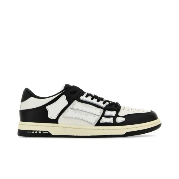 A pair of low top white and black sneakers by AMIRI available at Lestyle Boutique These sneakers feature skeleton inspired stitching designer logo details and a flat sole for comfort and a unique style