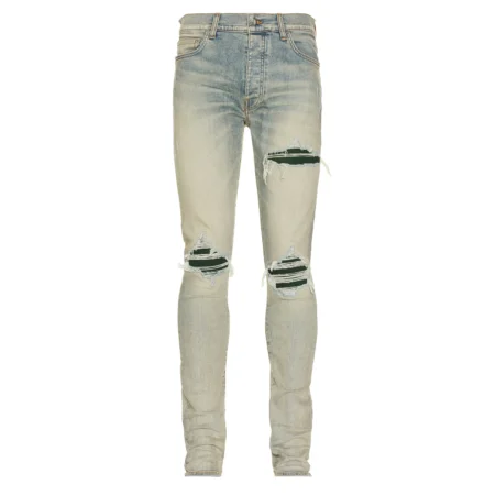 A pair of antiqued indigo stretch skinny jeans by AMIRI, available at Lestyle Boutique. These jeans feature a stonewashed and distressed finish, repaired rip details, and a contrasting logo metal plate for a bold, modern look.